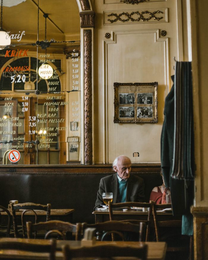 services-01 Elderly man sitting in a vintage Brussels cafe with wooden interiors and menu board.