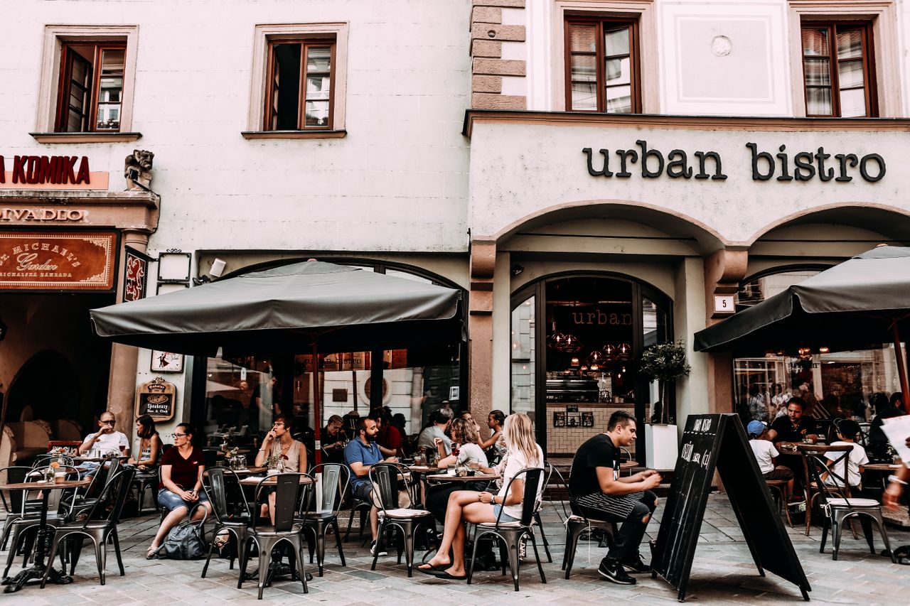 services-01 Exterior of modern cafe with people sitting at tables on sidewalk on first flour of residential building on city street at daytime